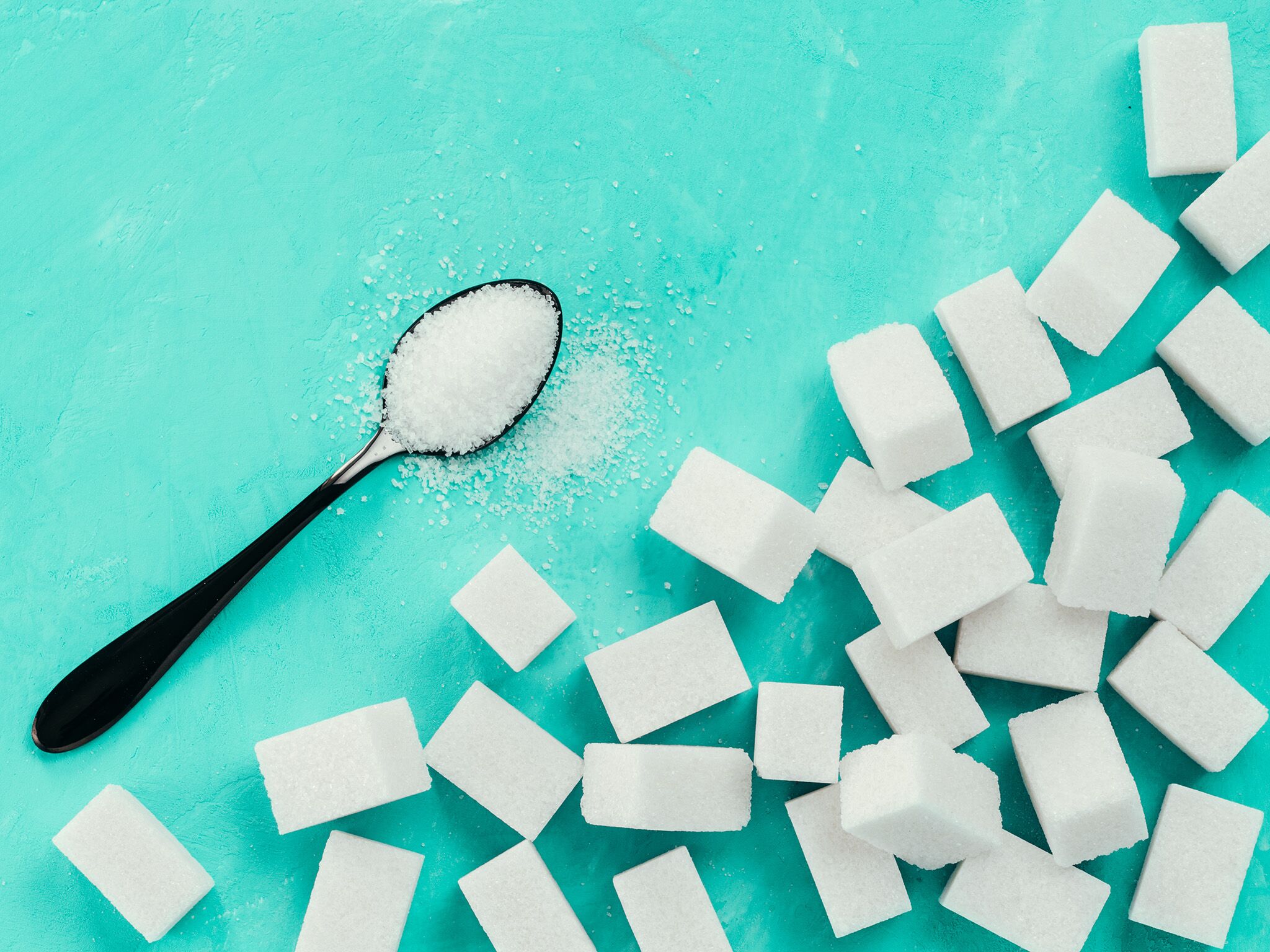 sugar-teaspoon-cubes-teal_708622288 sugar on a black teaspoon with sugar cubes piled nearby