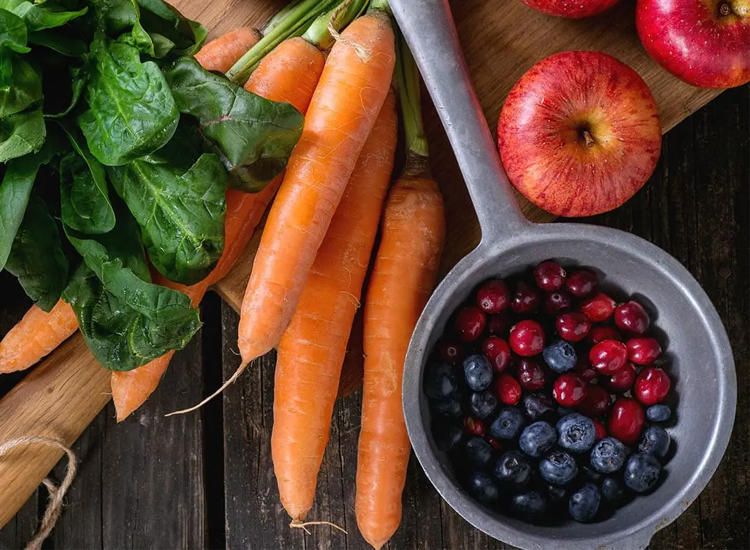 spinach, carrots, apples and berries laid out on a wooden table